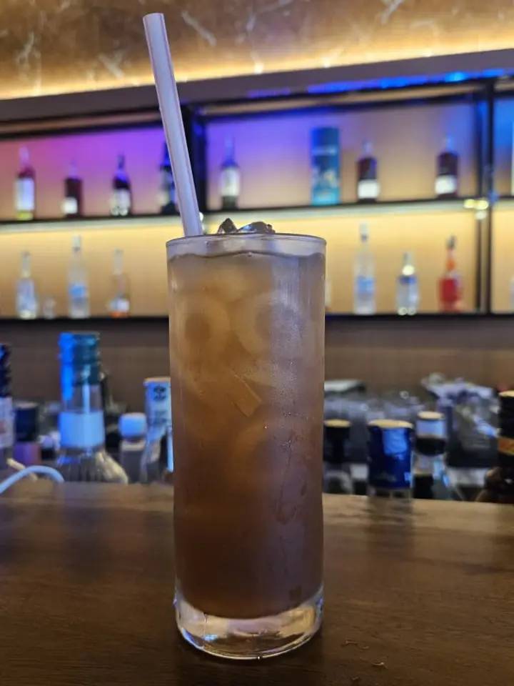 Tall iced drink with a straw against the glowing back bar