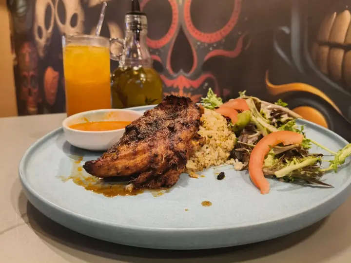 Grilled chicken with greens and a golden drink, skull mural background